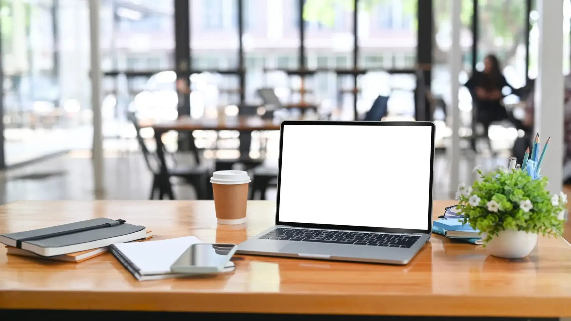 A laptop on a wooden desk with coffee, notebooks, and a plant in an office—typical workday setup in Charlotte.