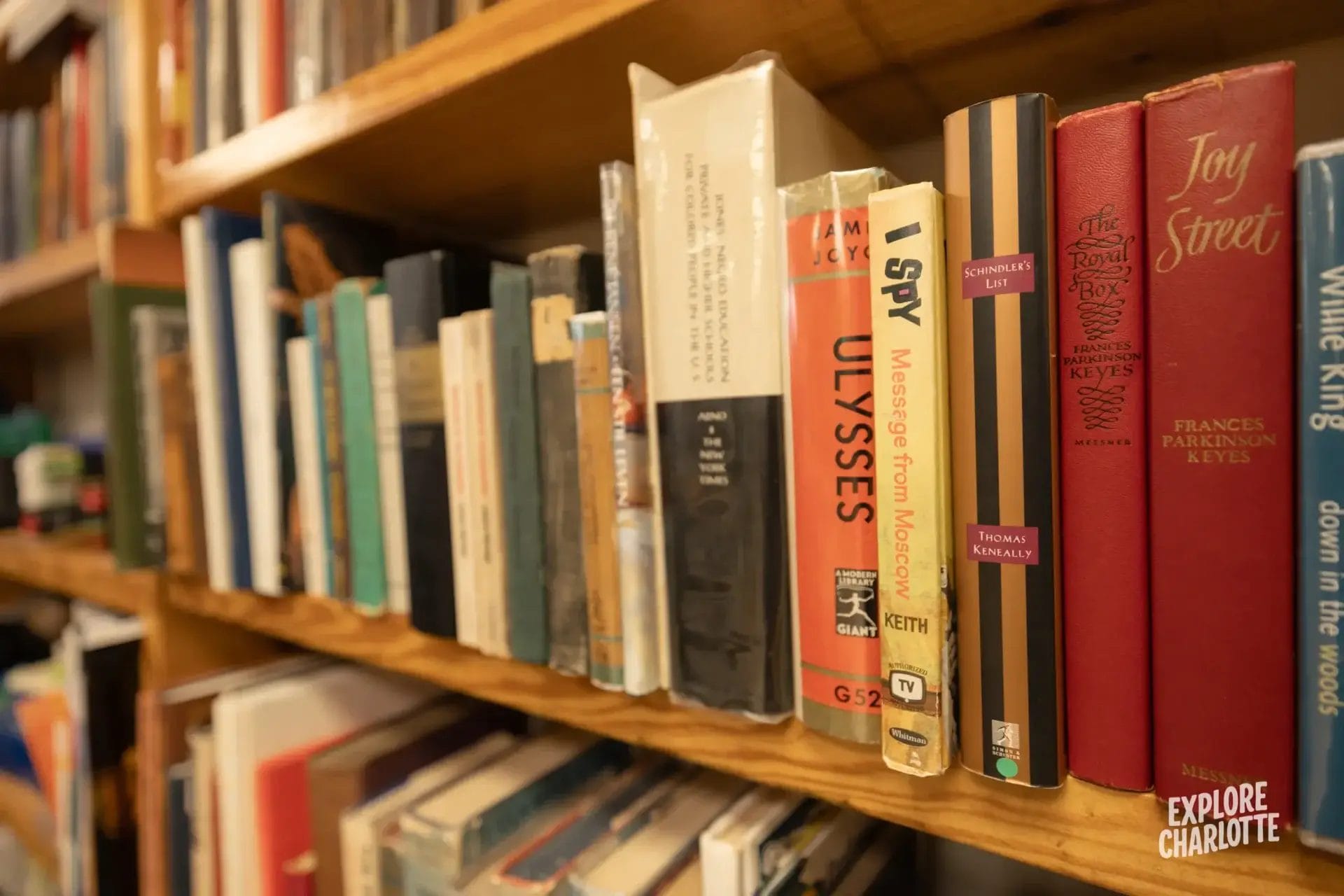Books like "Ulysses" and "Joy Street" on a shelf in a Charlotte bookstore, with an Explore Charlotte logo in the corner.