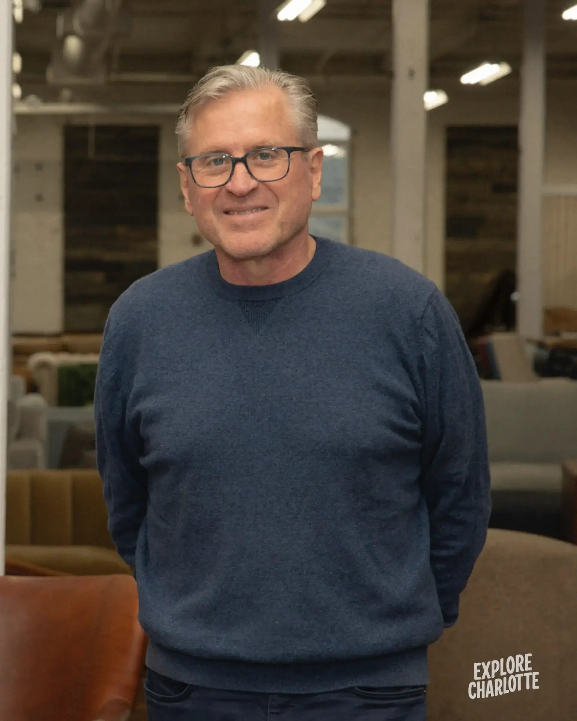 A man in glasses and a blue sweater stands inside COCOCOHome Furniture Store in Cornelius, with "Explore Charlotte" on the image.