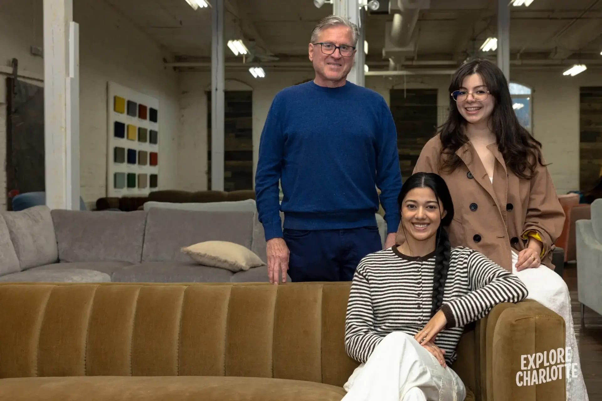Three locals smile together inside COCOCOHome in Charlotte, surrounded by modern couches and art in the showroom.
