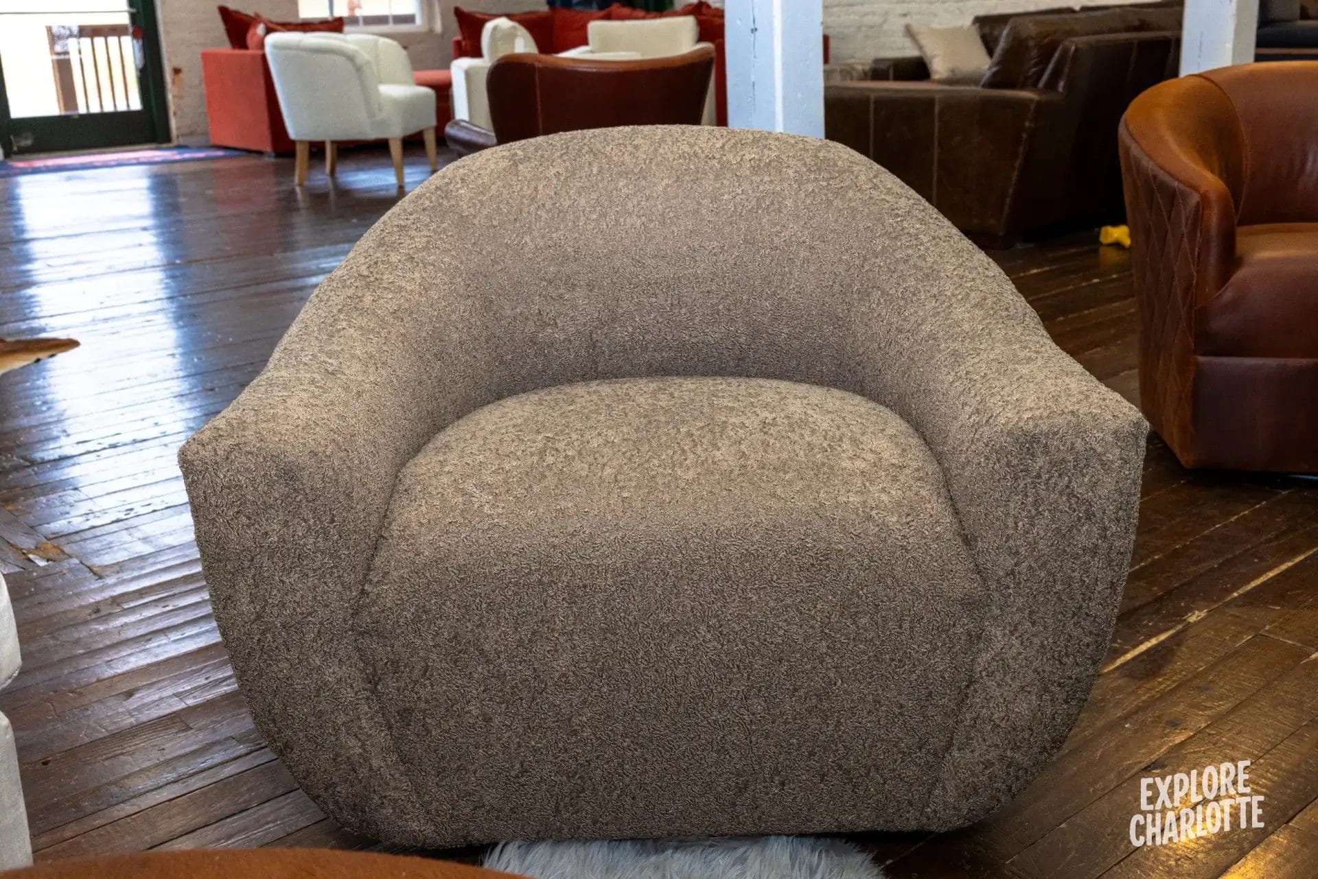 A gray armchair from COCOCOHome sits in a relaxed Charlotte lounge, with other seats nearby. "Explore Charlotte" logo at bottom.