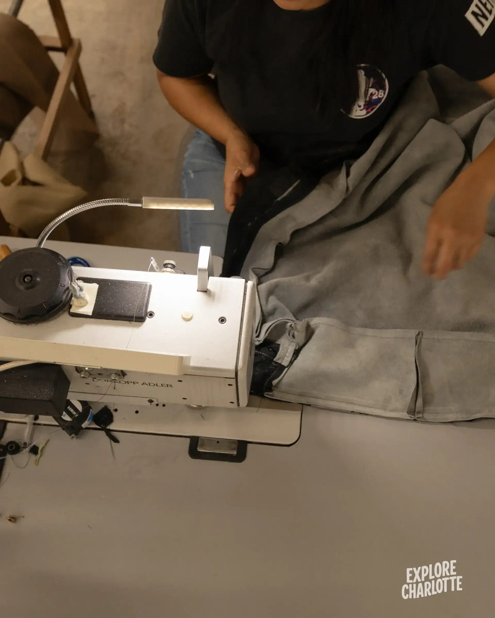 Someone sews grey fabric at a machine. "EXPLORE CHARLOTTE" and COCOCOHome Furniture Store Cornelius NC are shown below.