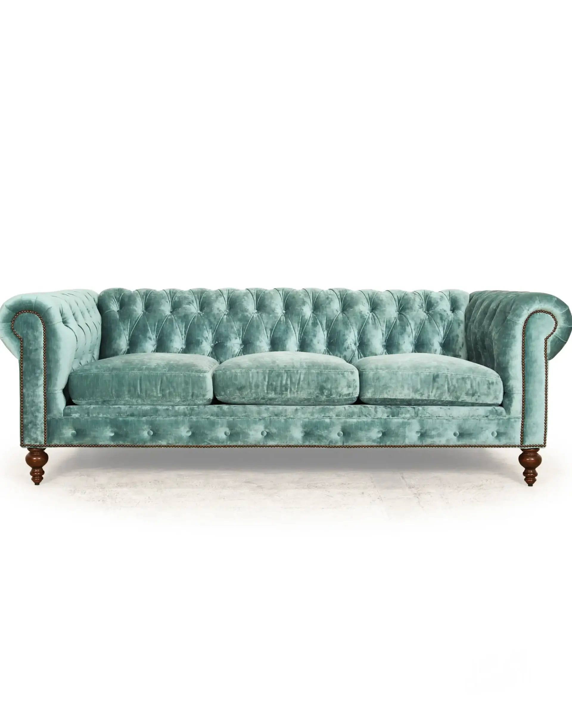 Teal velvet Chesterfield sofa from COCOCOHome in Cornelius, NC, with tufted buttons, rolled arms, and wooden legs on white background.